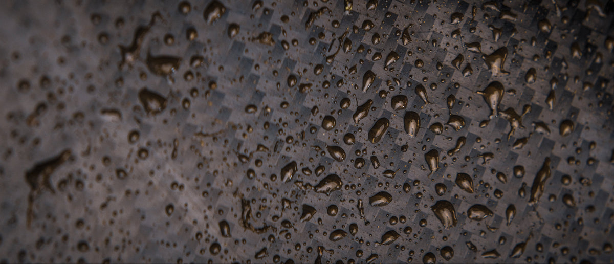 Close-up of a dark textured surface covered with small water droplets, showing a water-repellent or waterproof finish.